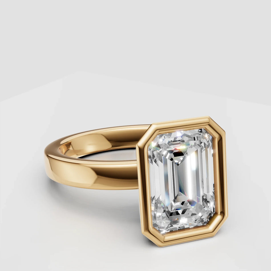 Emerald cut diamond engagement ring with yellow gold bezel setting on white background