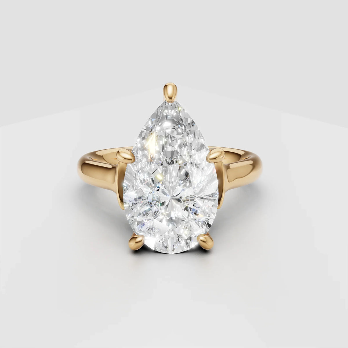 Pear-shaped diamond engagement ring with yellow gold band on white background
