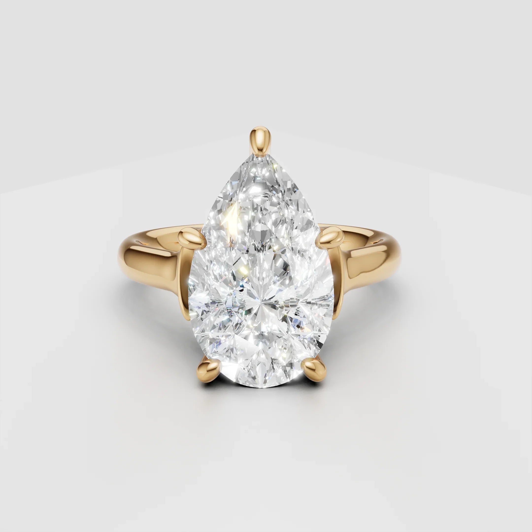 Pear-shaped diamond engagement ring with yellow gold band on white background