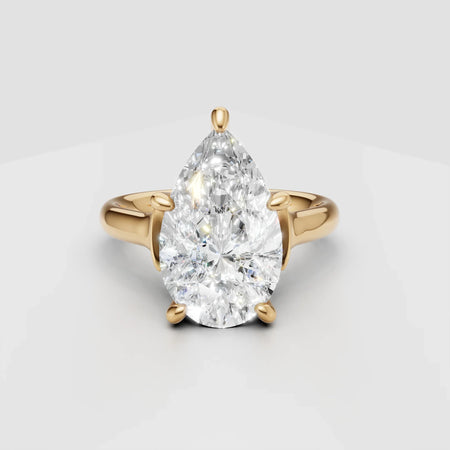 Pear-shaped diamond engagement ring with yellow gold band on white background