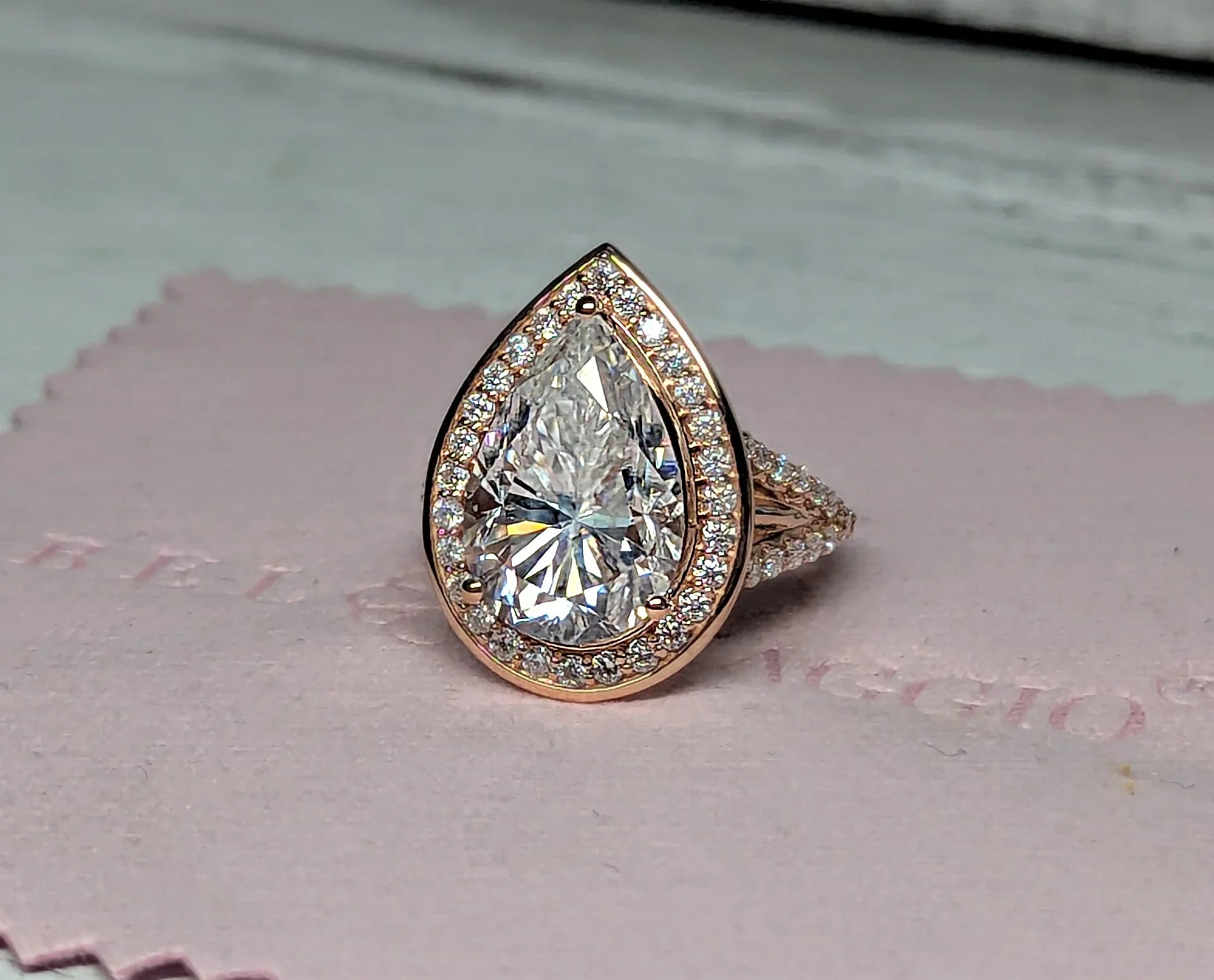 Pear-shaped diamond halo engagement ring with pavé band on pink jewelry cloth