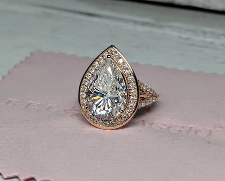 Pear-shaped diamond halo engagement ring with pavé band on pink jewelry cloth