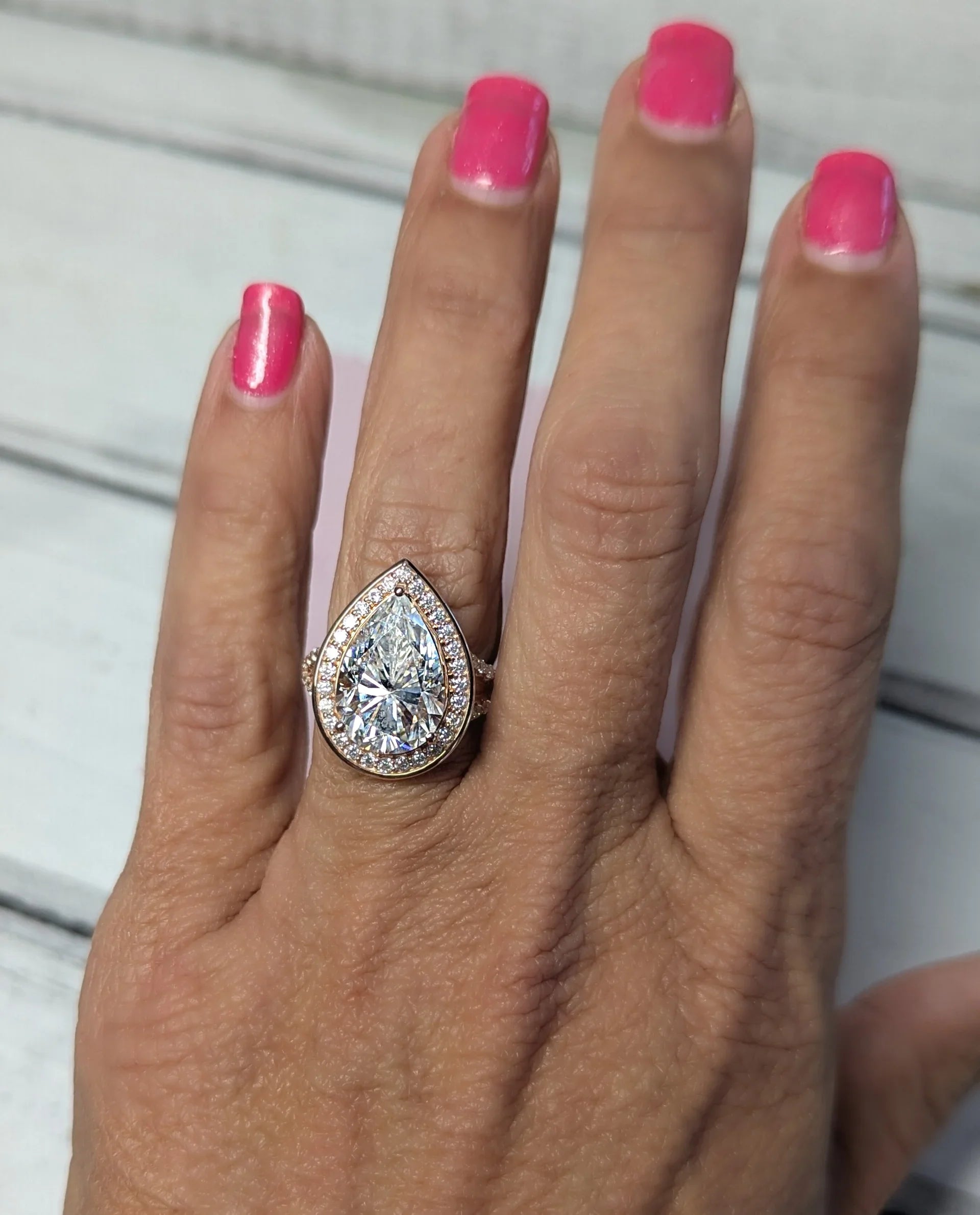 Pear-shaped halo diamond engagement ring with rose gold band on hand, pink manicure