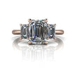 Three stone emerald cut diamond engagement ring with rose gold band on white background.
